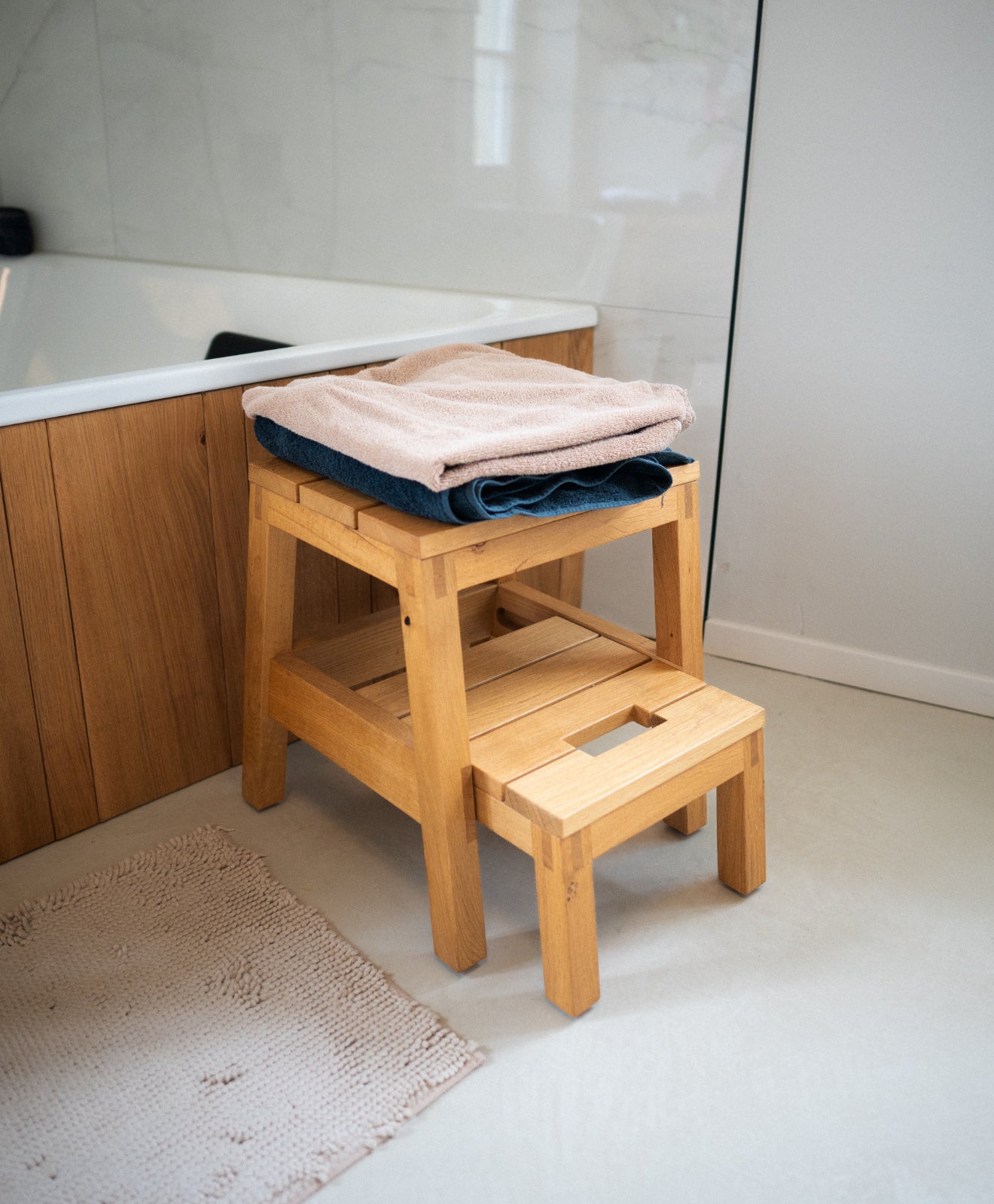 Tritthocker aus Holz (Eiche) Kurant von KAWENTSMANN im Badezimmer als Ablage von Handtücher zur Veranschaulichung des vielseitigen Einsatz des Tritthockers