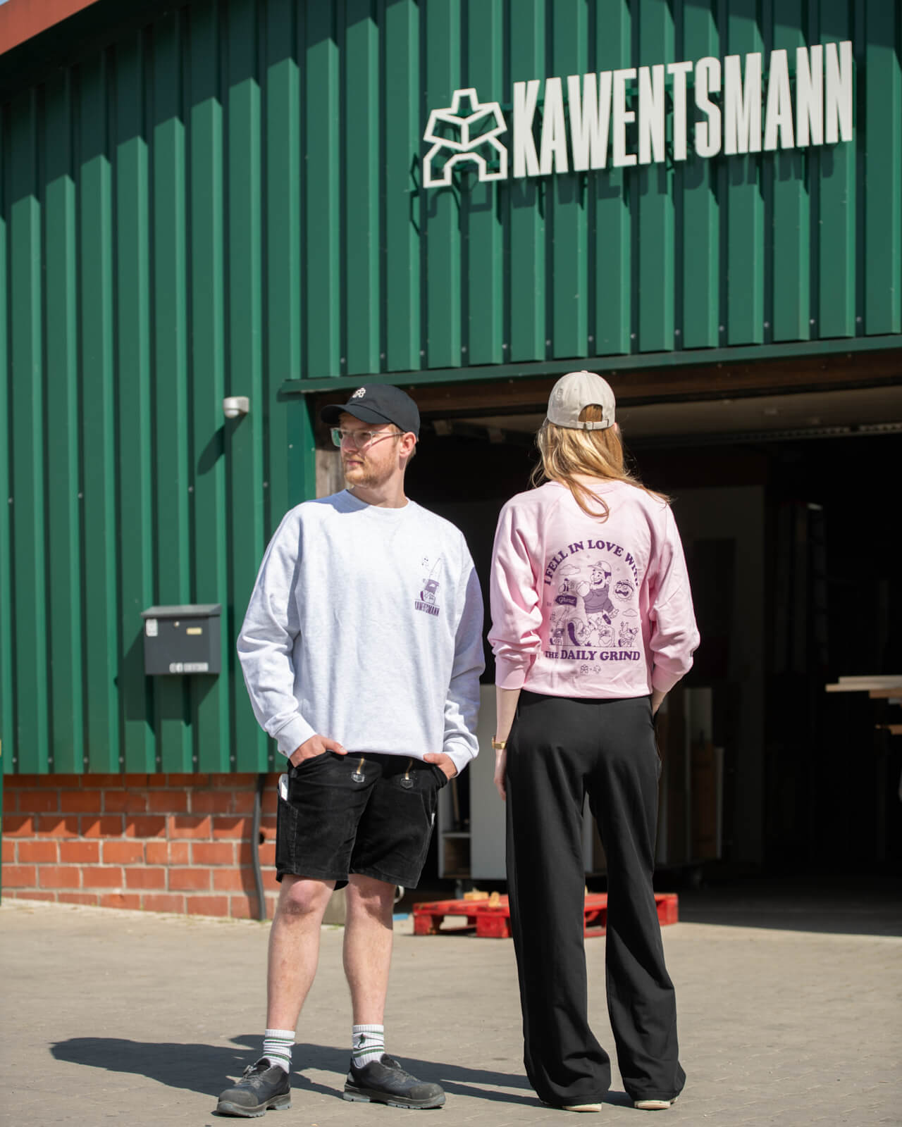 KAWENTSMANN Cap in Beige mit orangenem Logo-Stick und in Schwarz mit weißem Logo vor der Werkstatt