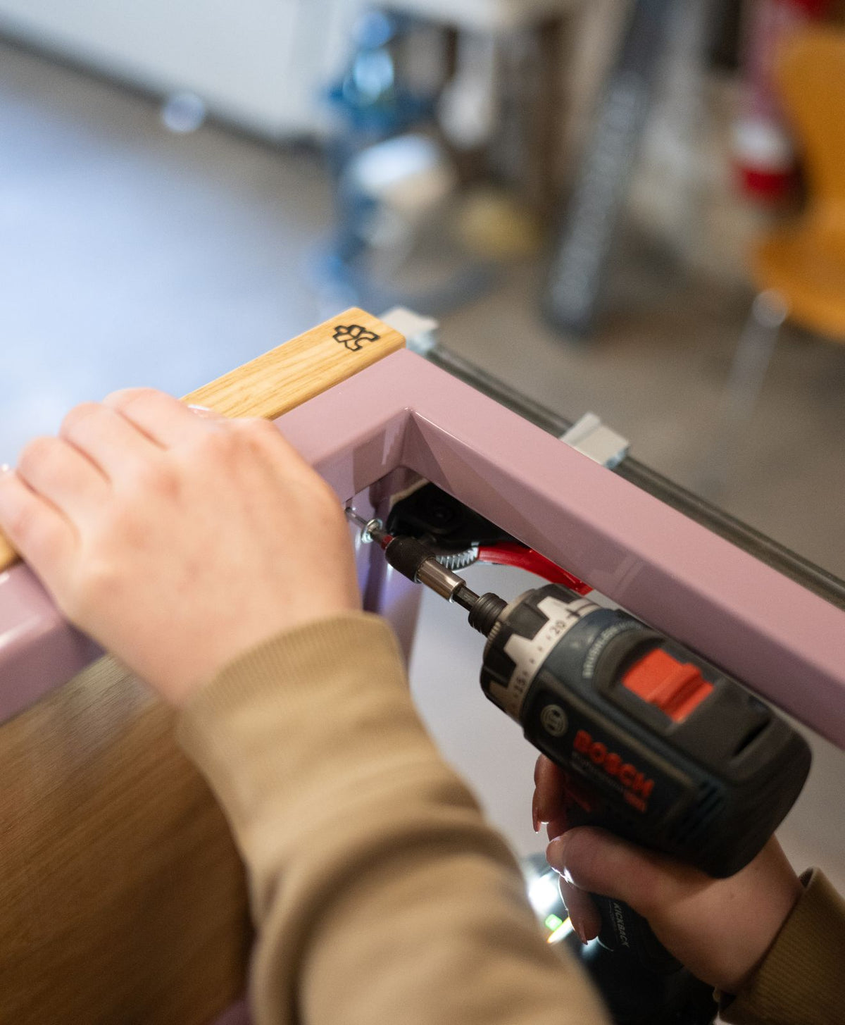 Mitarbeiterin von KAWENTSMANN verschraubt Holzplatte mit Stahlgestell zur Darstellung unserer Handarbeit