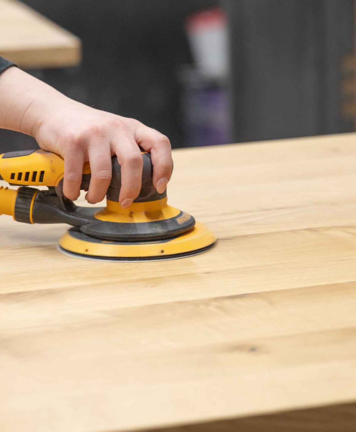 Mitarbeiterin von KAWENTSMANN schleift die Holzplatte für einen Vollholztisch zur Darstellung der Handarbeit mit Holz